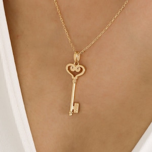 May include: A gold necklace with a heart-shaped key pendant. The key has a small inscription that reads "LOVE".
