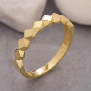 Könnte beinhalten: Ein goldener Bandring mit geometrischem Design. Die Band ist aus glattem, poliertem Gold gefertigt und verfügt über eine Reihe kleiner, spitzer Diamanten, die einen einzigartigen und modernen Look erzeugen.