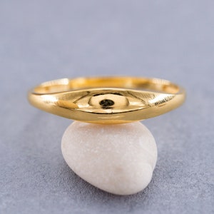 Op de afbeelding: Een eenvoudige gouden ring met een ronde band en een licht gewelfde bovenkant. De ring ligt op een witte steen.