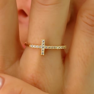 May include: A gold ring with a small cross design set with clear cubic zirconia stones.