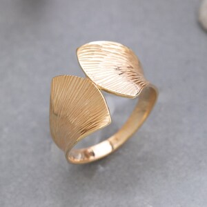 Puede incluir: Un anillo de oro con un diseño texturizado en forma de hoja. El anillo está abierto y tiene una banda ancha.
