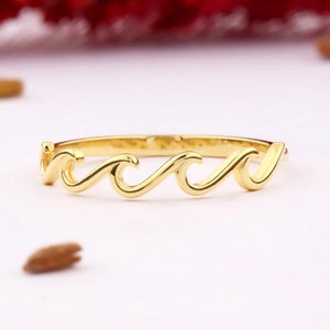 Op de afbeelding: Een gouden golfring met een eenvoudig ontwerp. De ring is gemaakt van een dunne band van metaal met drie golfvormen.