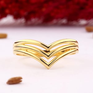 Könnte beinhalten: Ein goldener Ring mit einem dreifachen Chevron-Design. Der Ring ist aus glattem, glänzendem Metall.