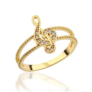May include: A gold ring featuring a treble clef design with clear cubic zirconia stones. The ring has a beaded band.