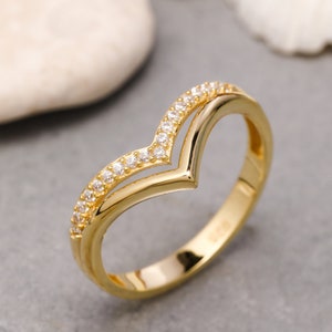 May include: A gold ring with a V-shaped design and small clear stones around the band.