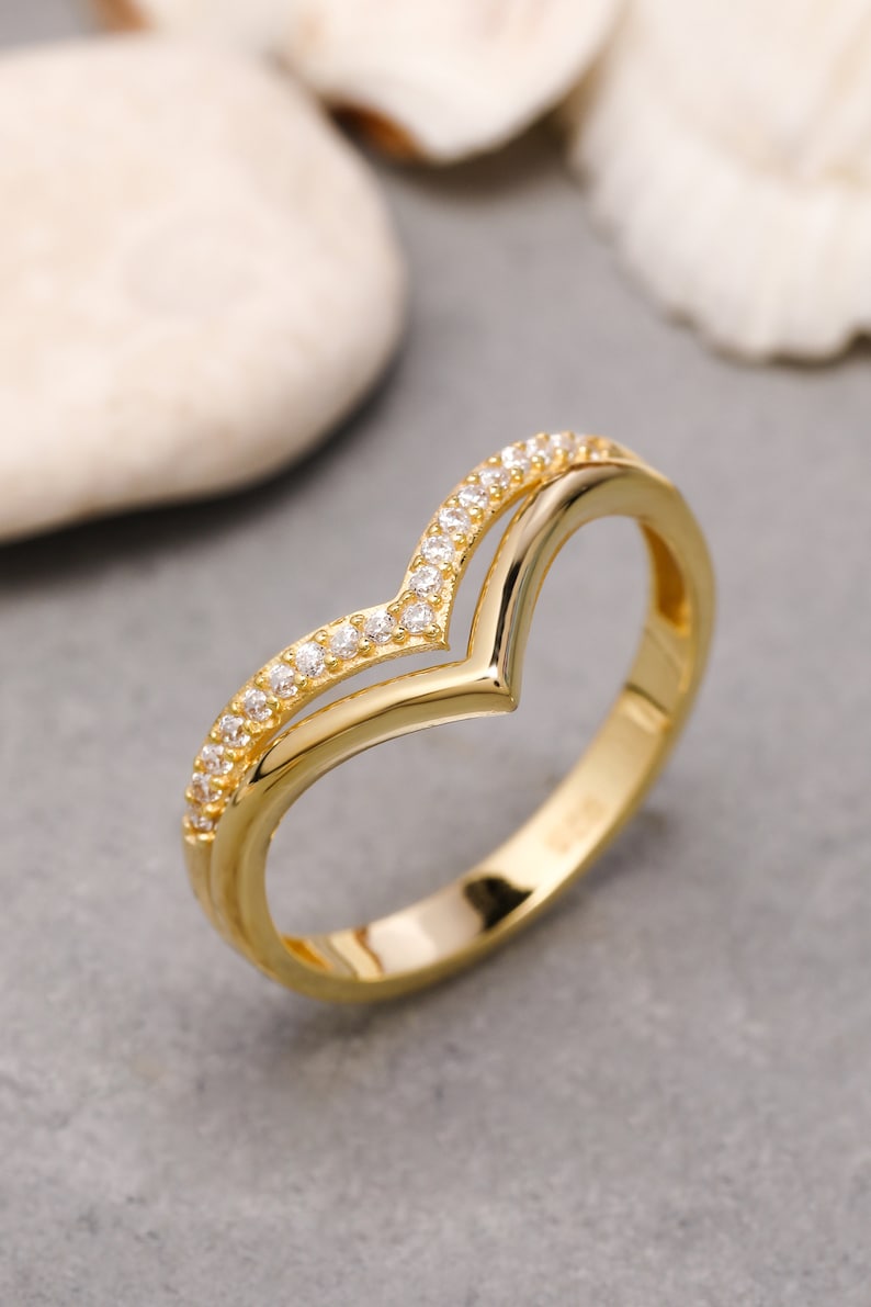 May include: A gold ring with a V-shaped design and small clear stones around the band.