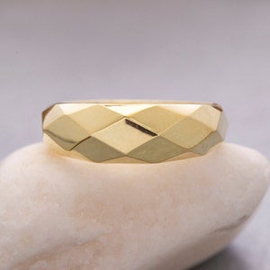 May include: A gold band ring with a geometric, faceted design. The ring is made of a shiny metal and has a smooth, polished finish.