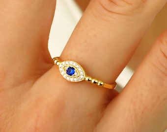 May include: Gold ring with a blue evil eye charm surrounded by clear cubic zirconia stones.
