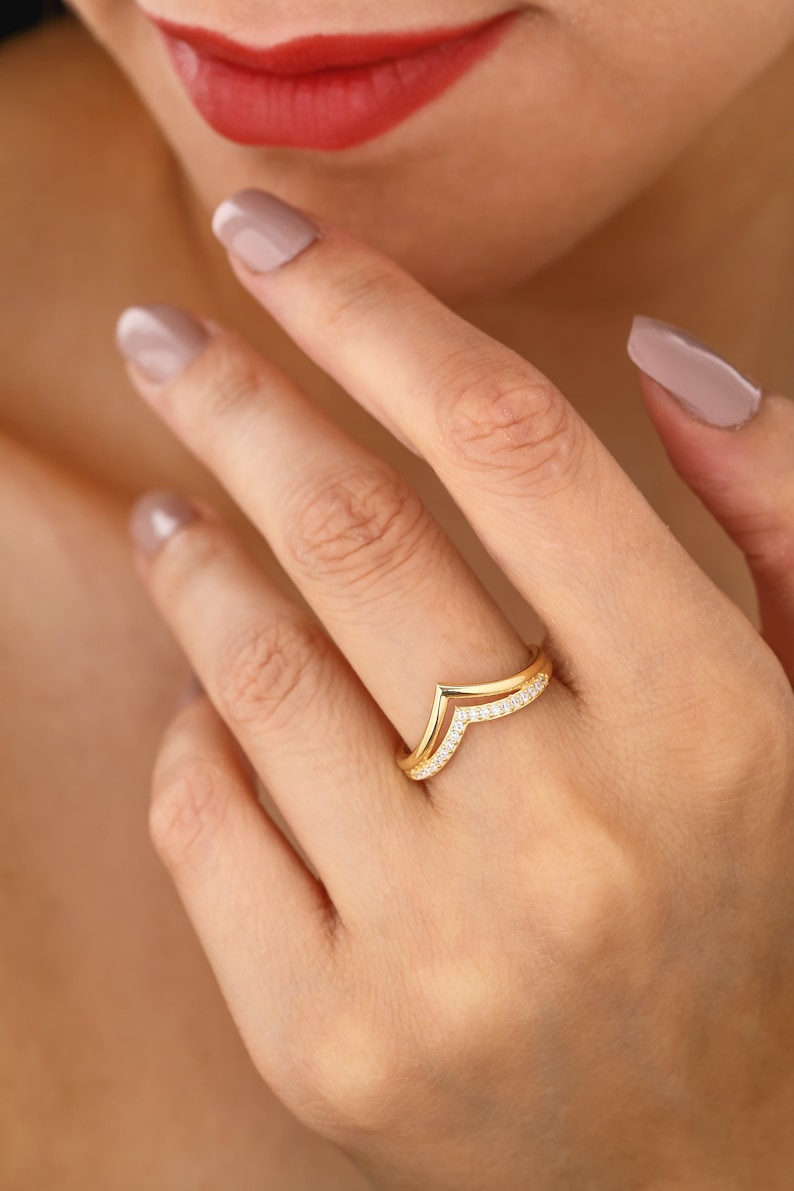 May include: A gold ring with a V-shaped design and small clear stones set in the band.