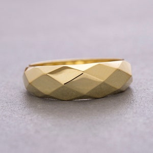 May include: A gold-colored ring with a geometric, faceted design. The ring is wide and has a rounded shape.