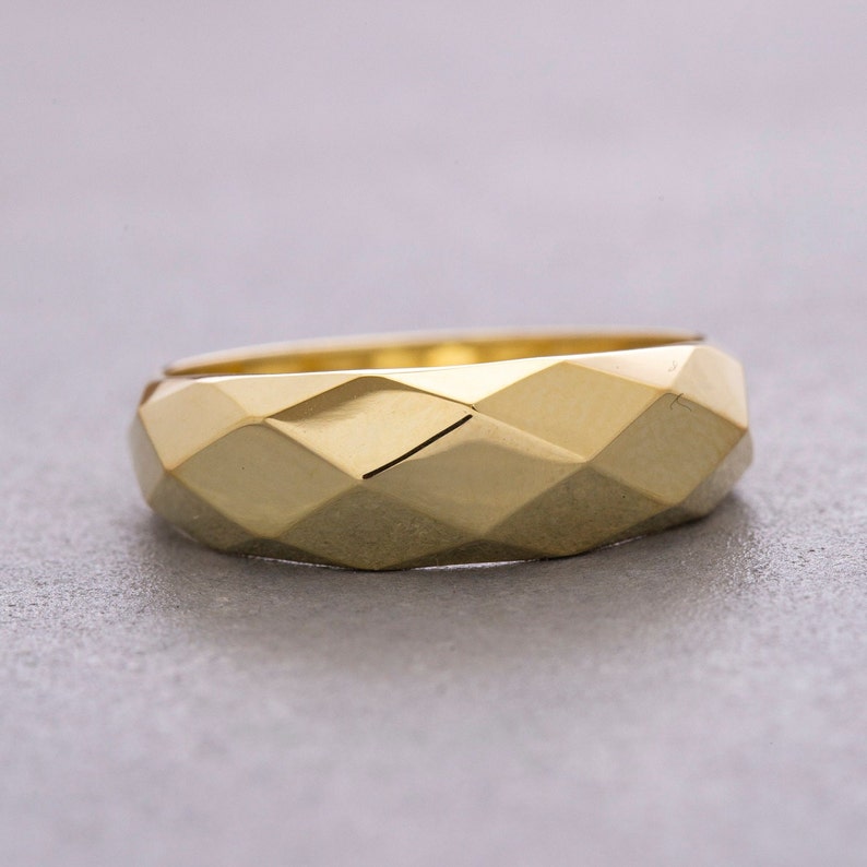 May include: A gold-colored ring with a geometric, faceted design. The ring is wide and has a rounded shape.