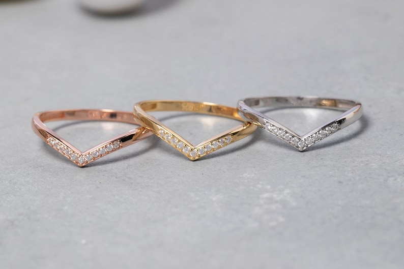 May include: Three V-shaped rings with a row of small diamonds set in the band. The rings are in rose gold, yellow gold, and silver.