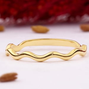 Può includere: Un semplice anello a fascia d'oro con un design ondulato. L'anello è realizzato in metallo liscio e lucido.