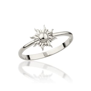 May include: A silver ring with a sun design. The sun is centered on the ring and has a raised, round center.