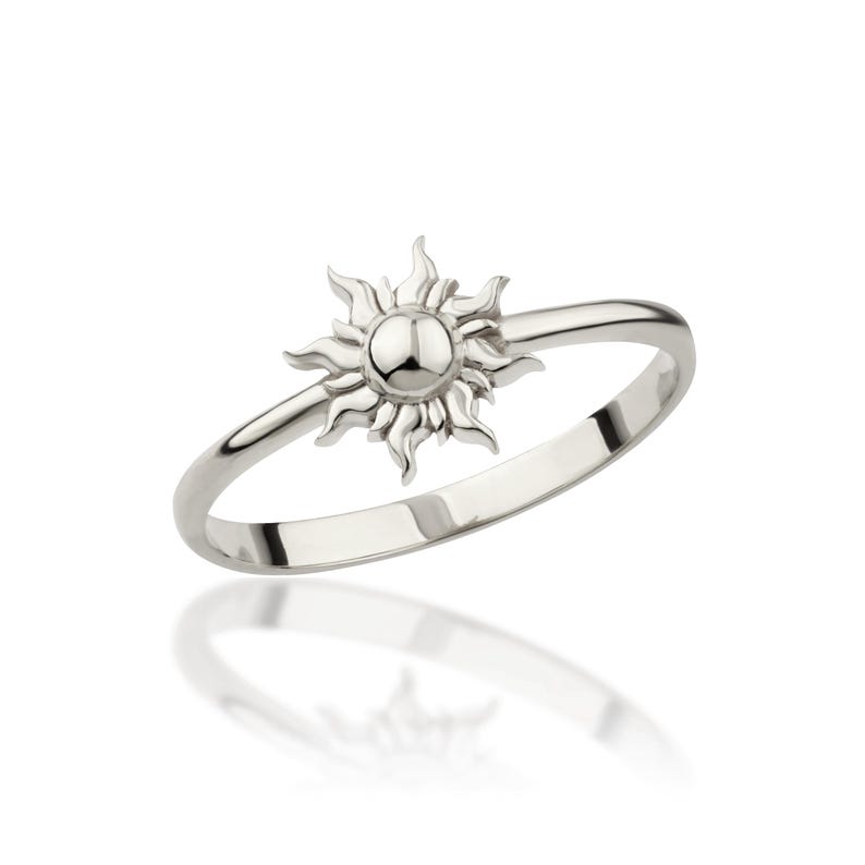 May include: A silver ring with a sun design. The sun is centered on the ring and has a raised, round center.