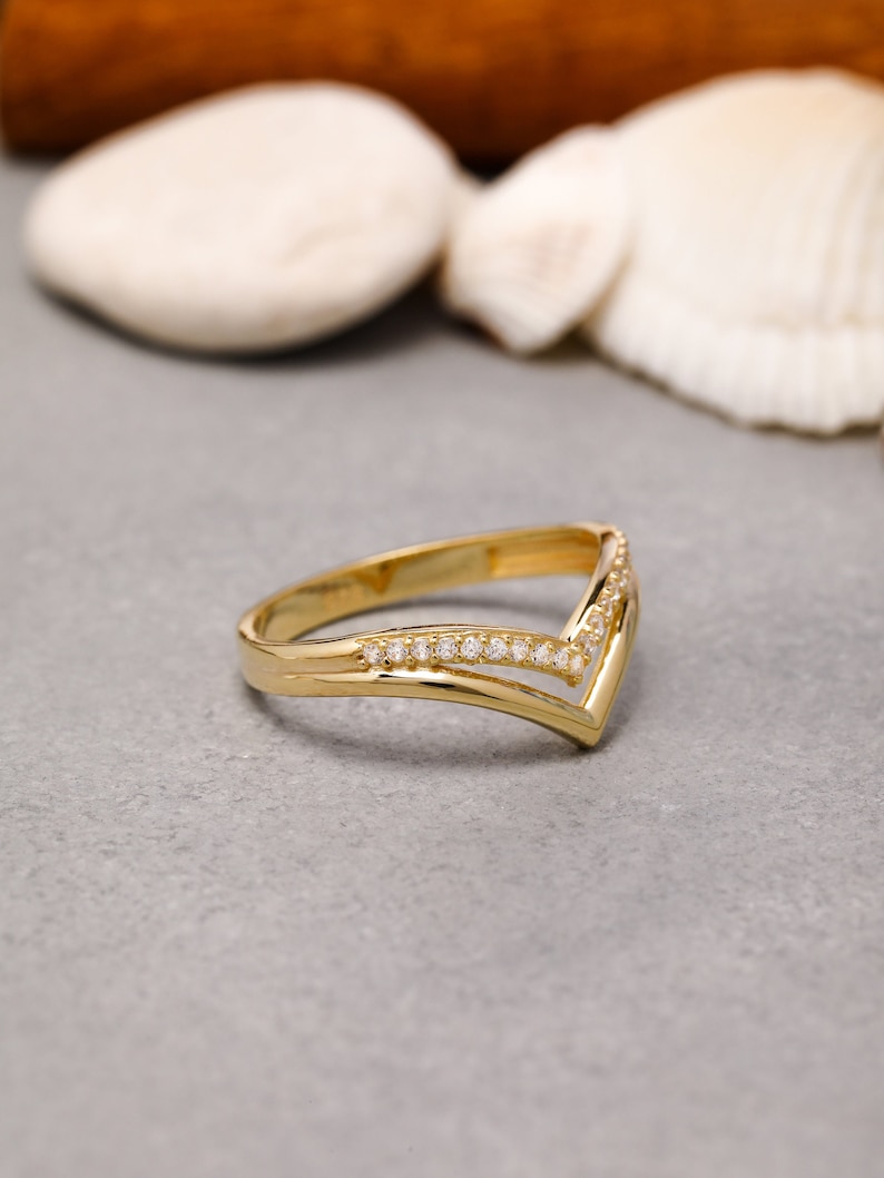 May include: A gold ring with a V-shaped design and small clear stones set in the band.