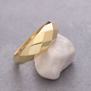 May include: A gold ring with a geometric, faceted design. The ring is sitting on a white stone.