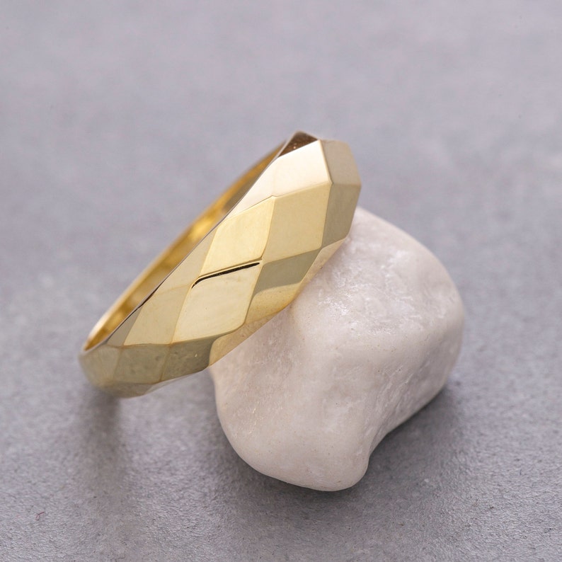 May include: A gold ring with a geometric, faceted design. The ring is sitting on a white stone.