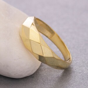 May include: A gold ring with a geometric, faceted design. The ring is polished and has a smooth, shiny finish.