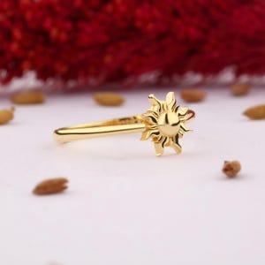 May include: A gold ring with a sun design. The ring is simple and delicate, with a smooth band and a raised sun design.