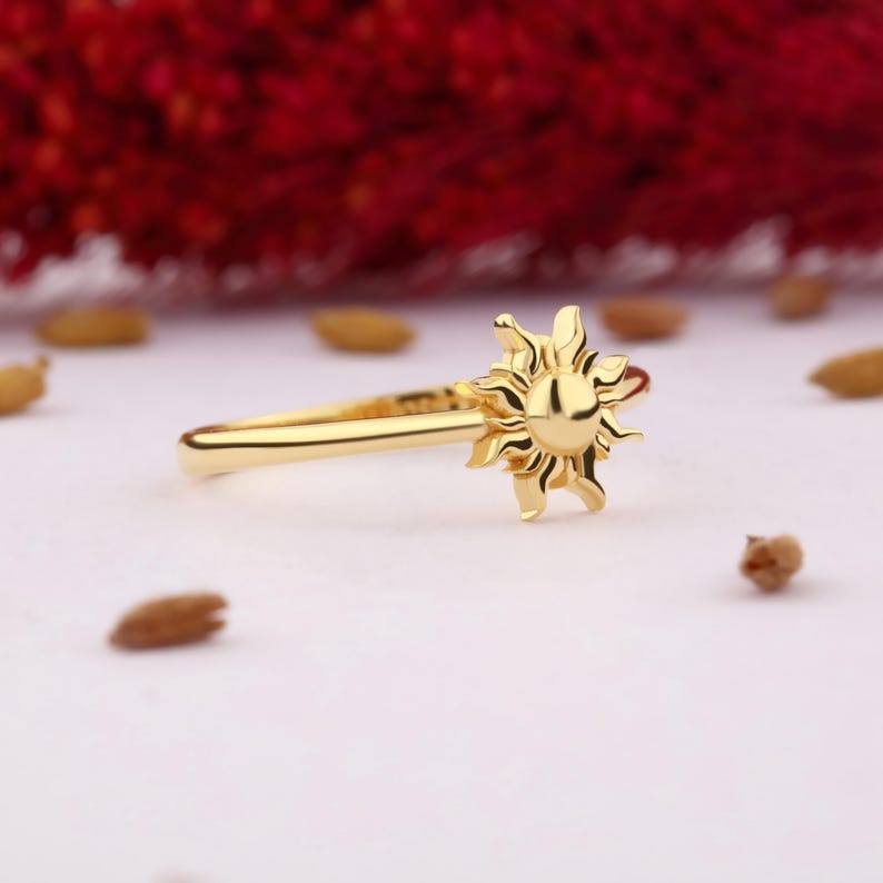 May include: A gold ring with a sun design. The ring is simple and delicate, with a smooth band and a raised sun design.