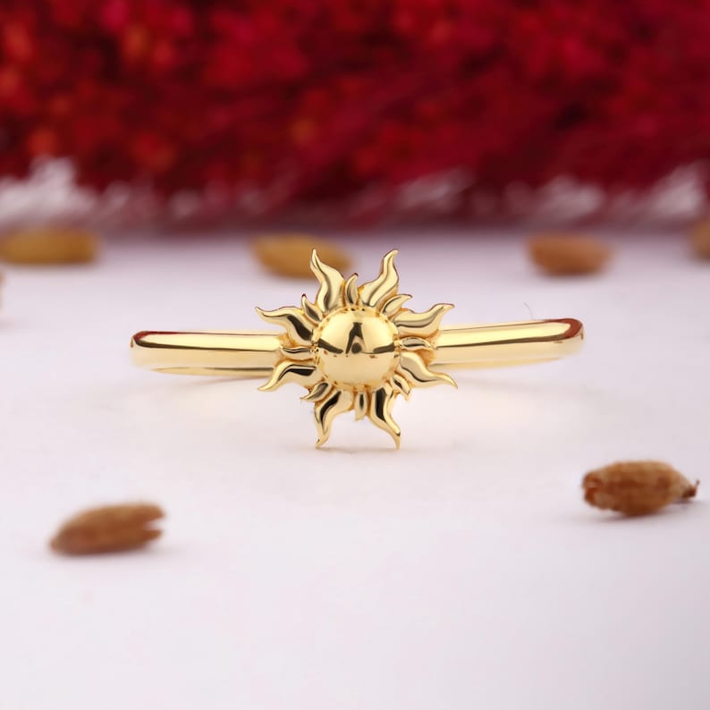 May include: A gold ring with a sun design. The sun is raised and has a textured surface.