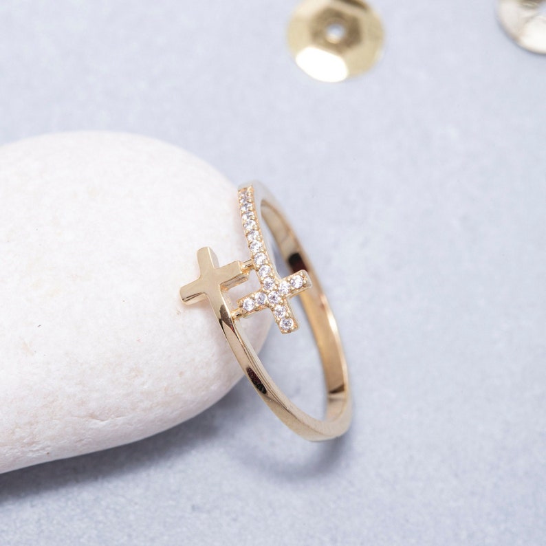 May include: A gold ring featuring two small crosses set with clear cubic zirconia stones.