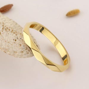 May include: A polished gold ring featuring a faceted, geometric band design. The ring has a smooth, reflective surface with multiple angled planes that create a distinct, multi-sided appearance. The metal is a bright, warm yellow gold tone.