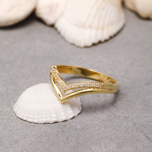 May include: A gold ring with a V-shaped design and small clear stones set in the band.