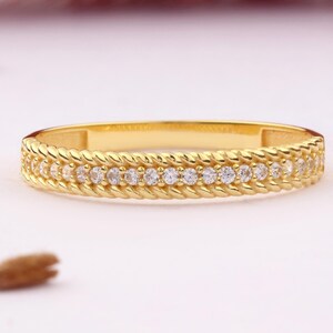 May include: A gold band ring with a braided design and a row of small clear stones.