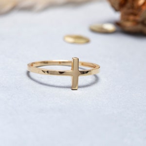 May include: A gold-toned ring featuring a simple cross design. The ring is made of metal and has a smooth finish.