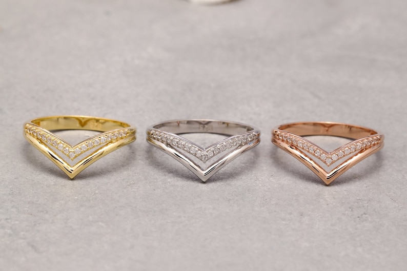 May include: Three gold, silver, and rose gold rings with a double V-shaped design and small clear stones.