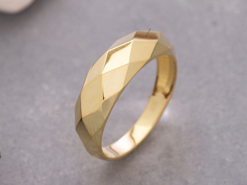 May include: A gold band ring with a geometric, faceted design.