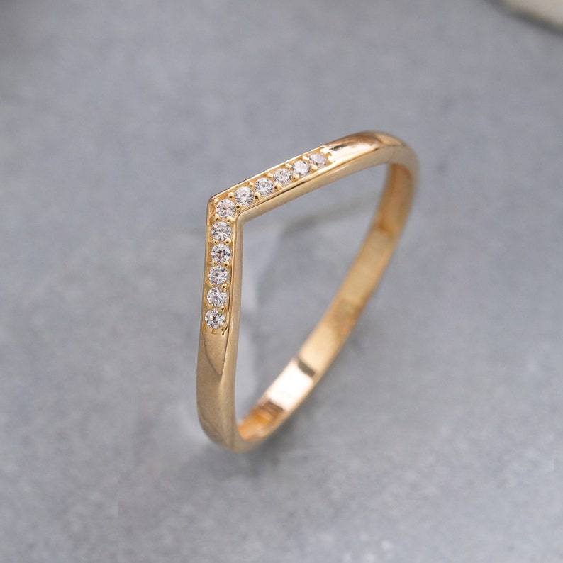 May include: A gold ring with a V-shaped band and small clear stones set along the top edge.