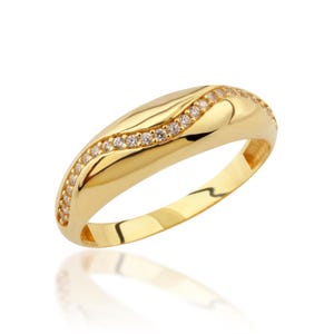 May include: A gold band ring with a row of small clear stones set in a curved line.