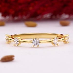 Puede incluir: Un delicado anillo de banda de oro con cinco pequeñas piedras redondas transparentes engastadas en garras. Las piedras están espaciadas uniformemente a lo largo de la banda.