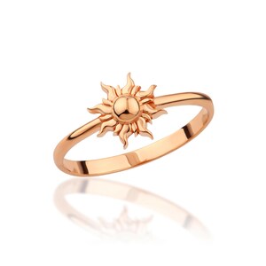 May include: A rose gold ring with a sun design. The sun is detailed with rays and a round center.
