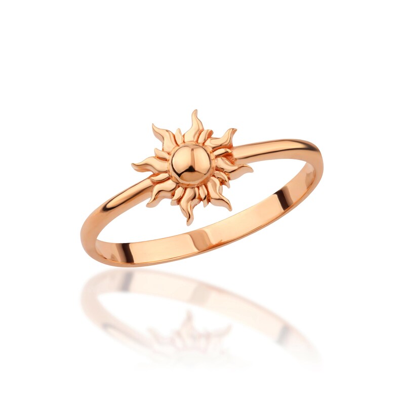 May include: A rose gold ring with a sun design. The sun is detailed with rays and a round center.
