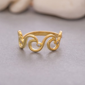 May include: A gold ring with a wave-like design and two small clear stones.