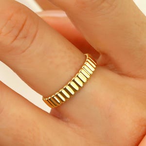May include: A gold ring with a textured, ridged design. The ring is worn on a finger.