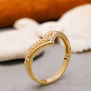 May include: A gold ring with a V-shaped design and small clear stones set along the band.