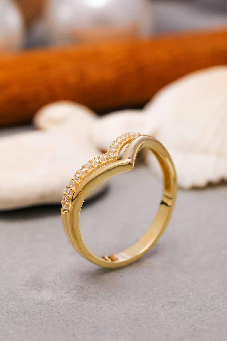 May include: A gold ring with a V-shaped design and small clear stones set along the band.