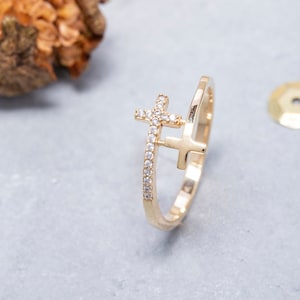 May include: A gold ring featuring a double cross design. The cross is set with small clear stones.