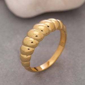 May include: A gold ring with a textured, rounded band. The band is made up of a series of small, rounded bumps.