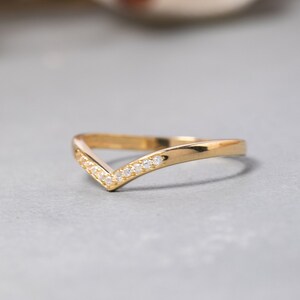 May include: A gold band ring with a V-shaped design and small clear stones set along the edge.