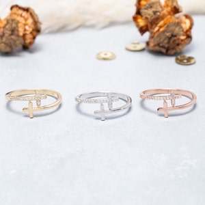 May include: Three delicate rings featuring a cross design. The rings are crafted from gold, silver, and rose gold. Each cross is embellished with small sparkling stones.