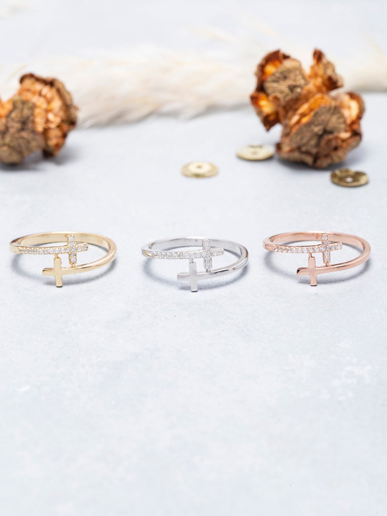 May include: Three delicate rings featuring a cross design. The rings are crafted from gold, silver, and rose gold. Each cross is embellished with small sparkling stones.