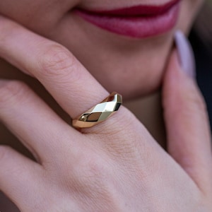 May include: A gold ring with a faceted design. The ring is worn on the finger of a person's hand.