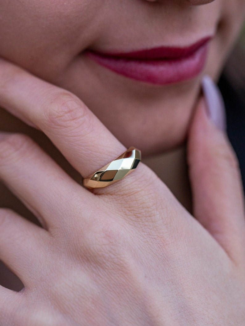May include: A gold ring with a faceted design. The ring is worn on the finger of a person's hand.