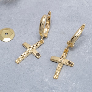 May include: A pair of gold hoop earrings with a cross pendant. The cross has a textured design.